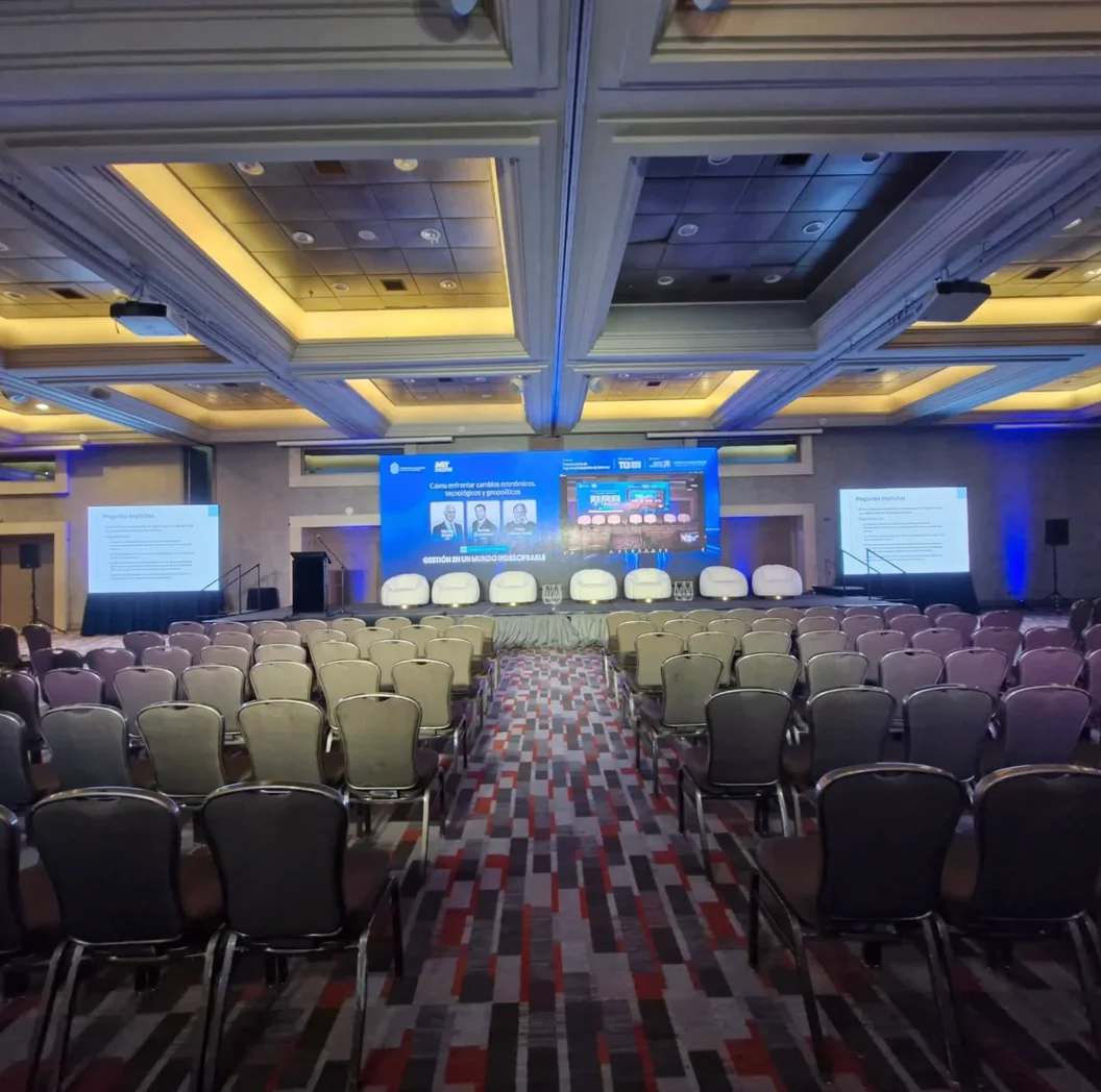 Salón corporativo con escenario, pantallas y sillas preparadas para los asistentes
